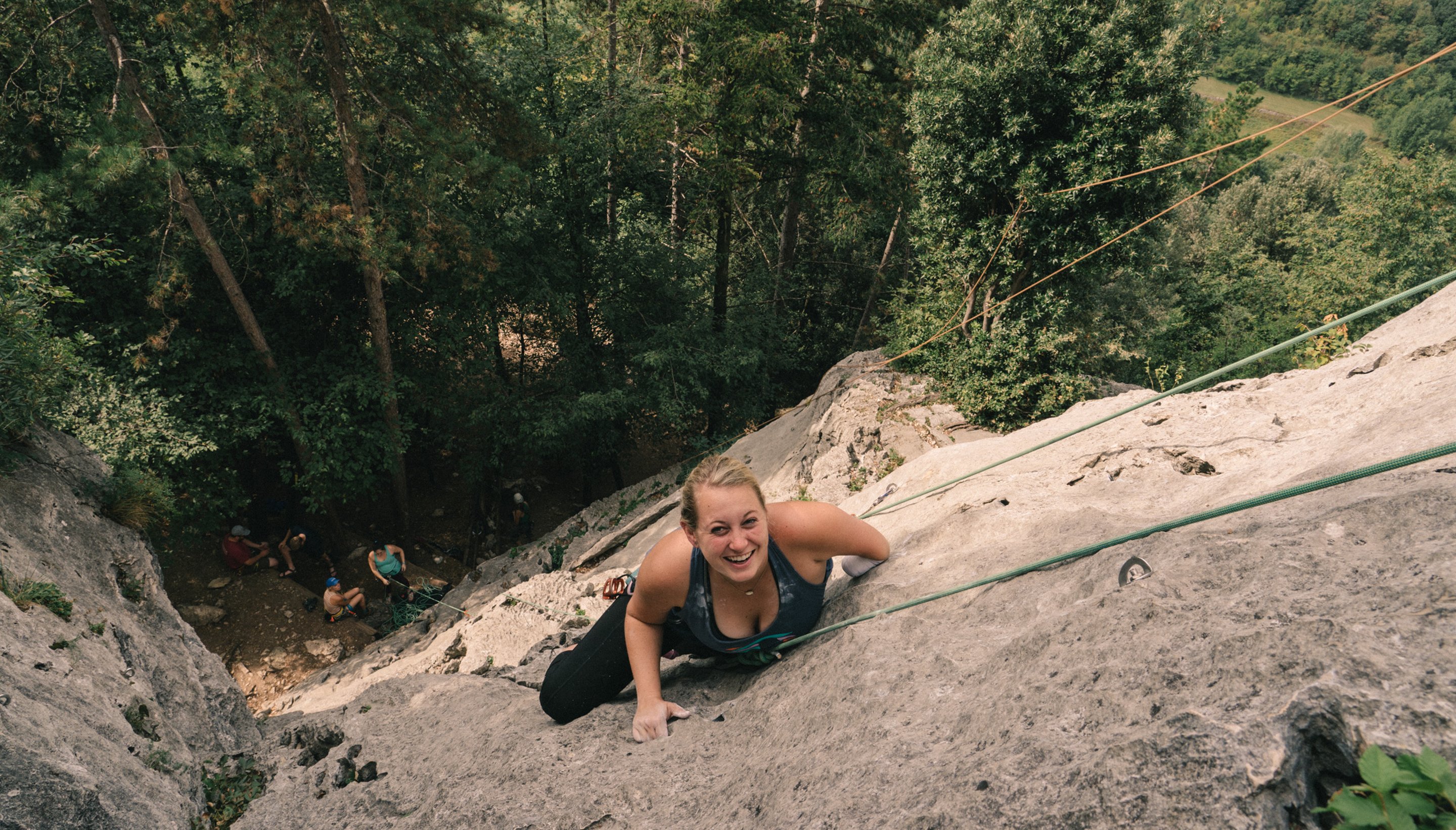 An amateur female climber smiles as she reaches the top of a wall.