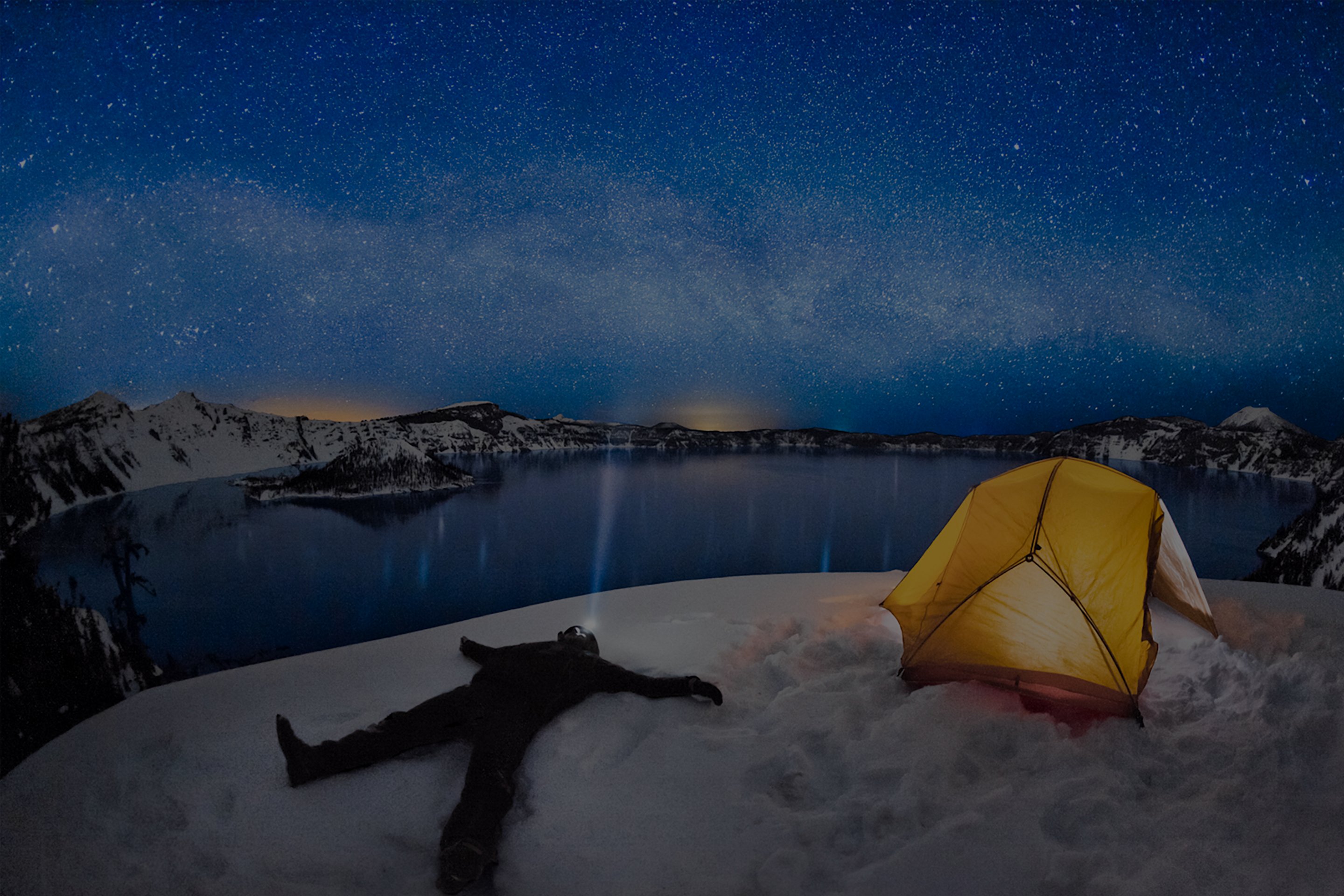 A winter camper gazes at a clear night sky while overlooking Crater Lake.