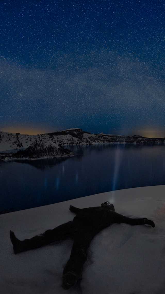 A winter camper gazes at a clear night sky while overlooking Crater Lake.