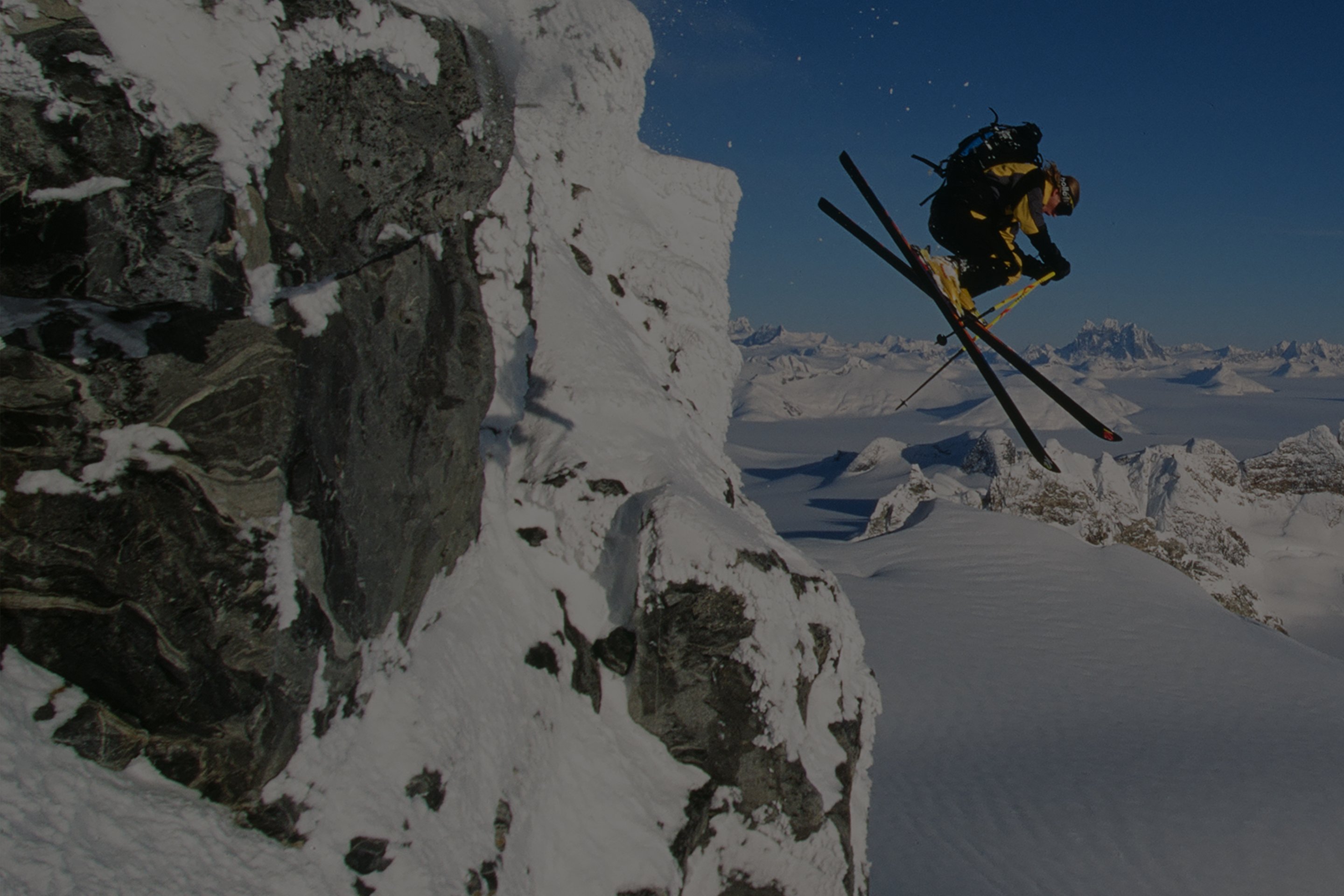 A skier makes a daring jump off a high alpine ledge.