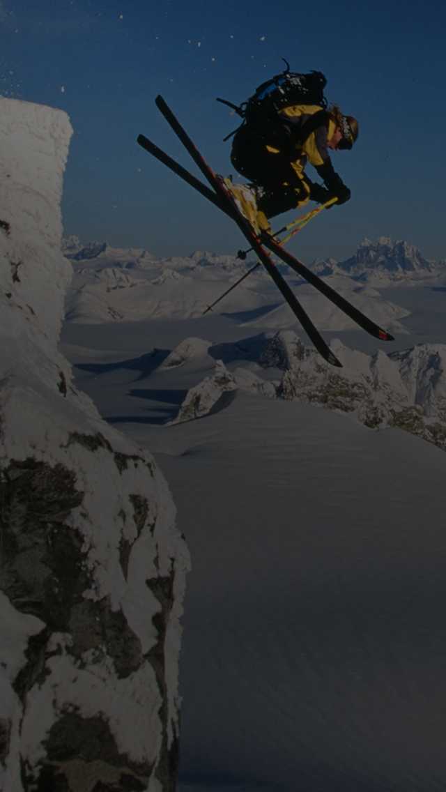 A skier makes a daring jump off a high alpine ledge.
