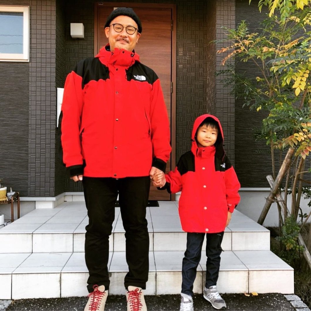 A man and a child pose together in front of an entryway wearing matching red The North Face jackets.