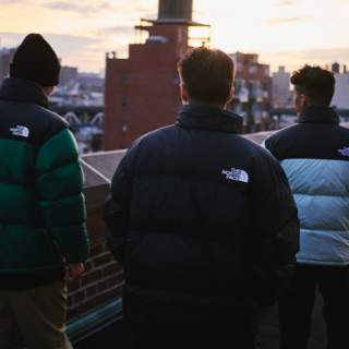 Trois personnes portant des manteaux Nuptse de The North Face se tiennent sur un toit dans une ville.
