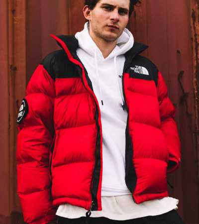 A man is wearing a red ’92 Nuptse from The North Face on a city rooftop at sunset.